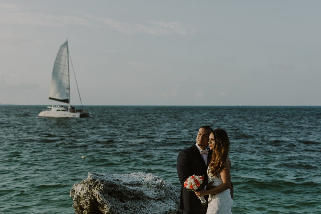 Bride and groom beach portraits with sailboat. Riu Caribe Cancun wedding by Caro Navarro Photography
